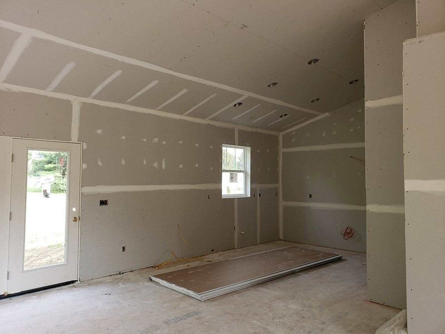 Bright room with white plaster walls, large windows, light wood flooring, and a door featuring a glass pane.