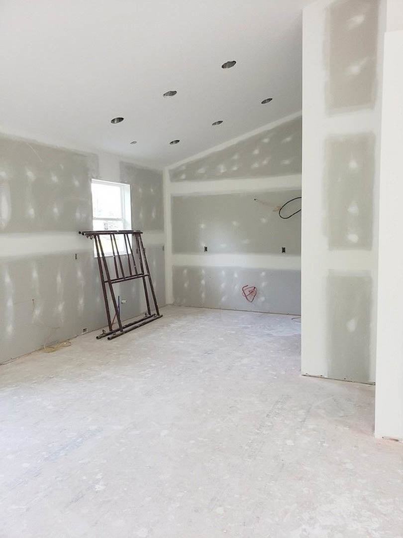 White-walled room with metal ladder leaning against plaster wall, white floor featuring a red wire, ceiling with small holes, and black circular detail on white surface.