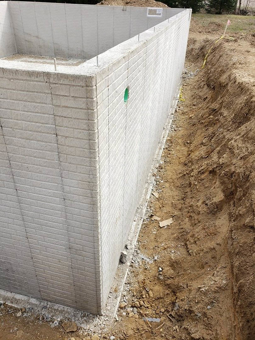 Concrete exterior wall with exposed hole in ground, loose soil, and yellow rope nearby