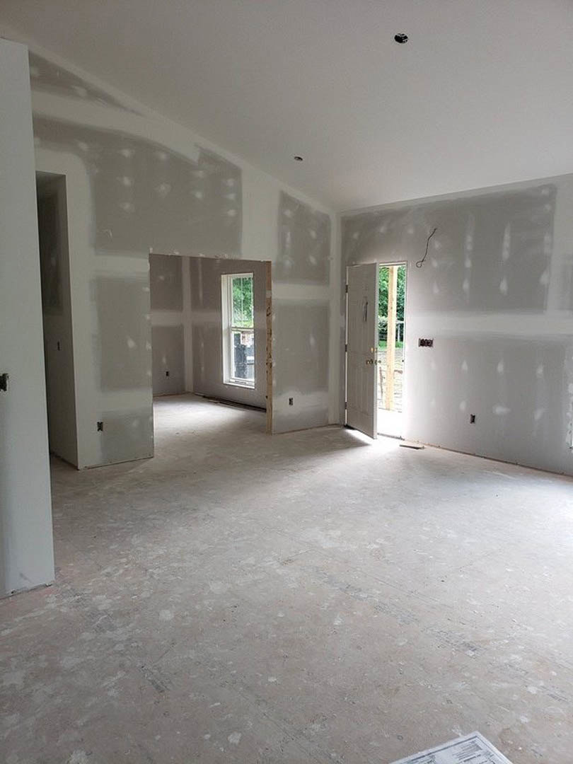 White plaster walls, open white door, light wood flooring, window with green foliage visible outside