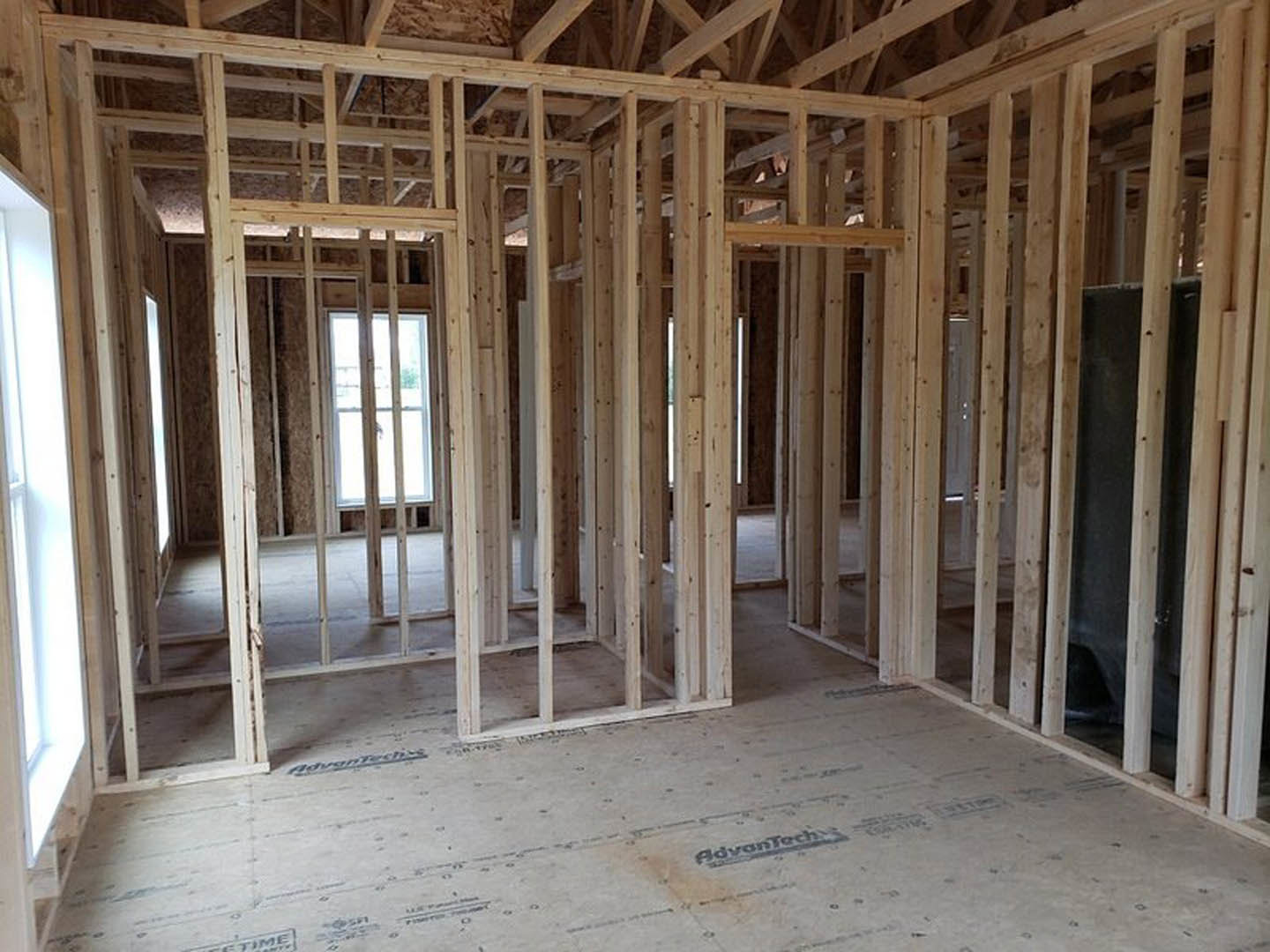 Unfinished room with exposed wood framing, visible ceiling beams, window opening, and construction materials on floor