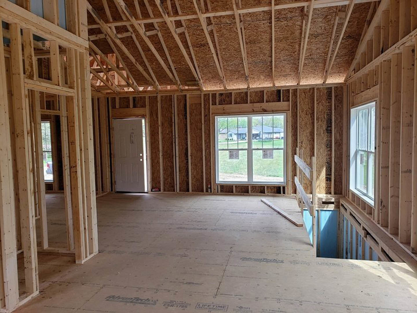 Wood plank flooring and exposed ceiling beams in a bright room with a white-framed window and a white door, natural light streaming through both.