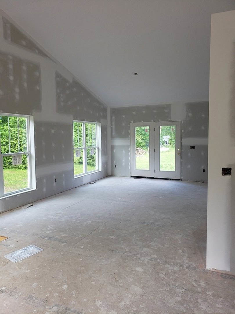 Bright room with smooth white walls, multiple windows with white frames, double glass-paneled doors, concrete floor, and a rectangular white fixture.