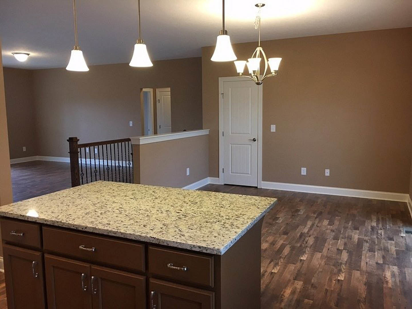 Brown wood kitchen island with matching cabinets, white countertop, silver drawer handles, wood flooring, white wall, and white door with silver handle.