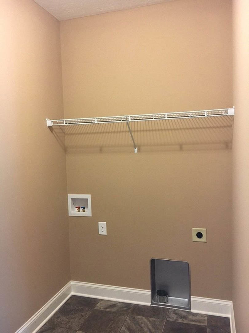 White tile floor and plaster wall in bathroom with built-in shelf holding metal object, white clothes rack, and wall-mounted fixture featuring red and blue handles.