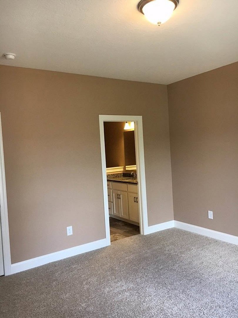 Beige-walled room with white door, carpeted floor, white kitchen cabinets, marble countertops, and modern light fixture