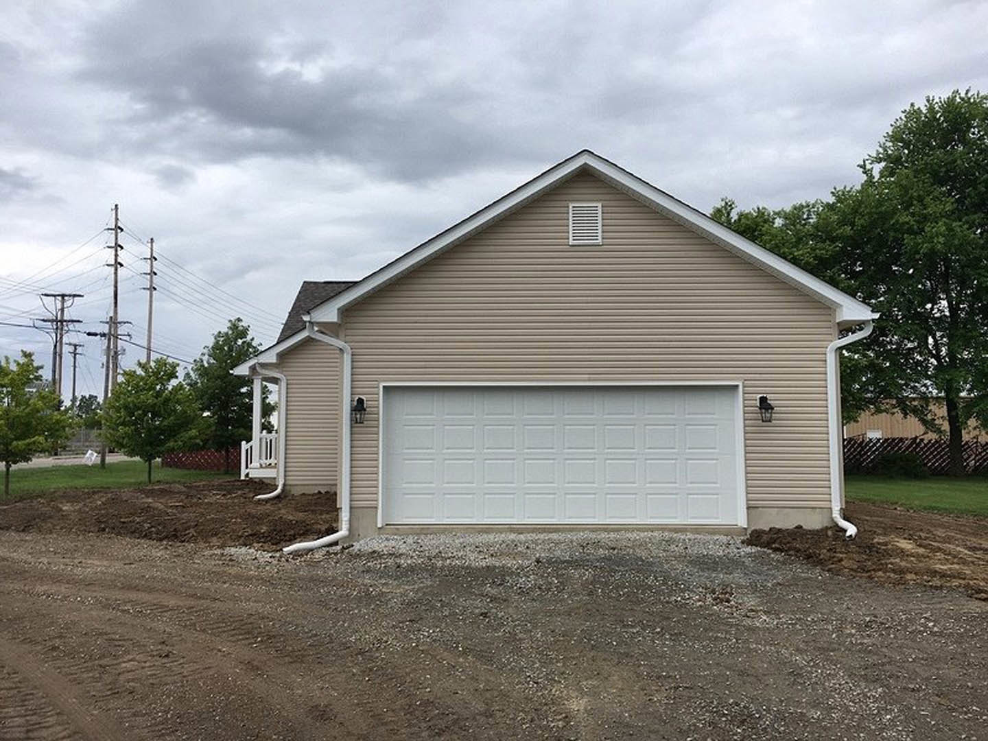 Brown-sided house with attached white garage door, white vent above, green-leaved tree nearby, cloudy sky, American Gothic House visible in background