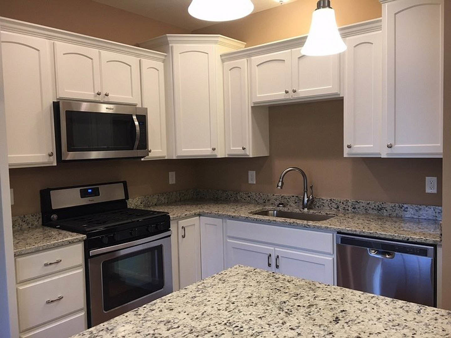 Granite countertops, white shaker cabinets, stainless steel appliances including microwave, stove, dishwasher, chrome faucet, and neutral tile backsplash in a modern kitchen