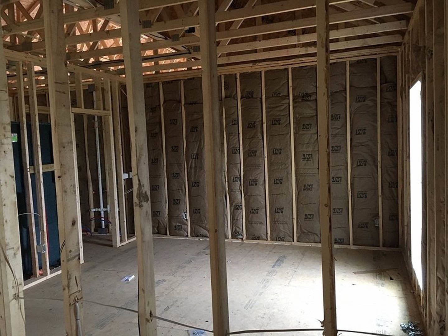 Exposed wood ceiling beams above a room with a wall covered in paper insulation, unfinished construction materials visible.