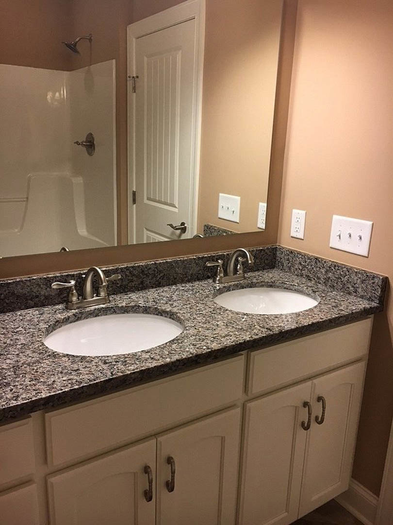 Granite countertop bathroom vanity with undermount sink, chrome faucet, large wall mirror, and white backsplash bordered in black tile.