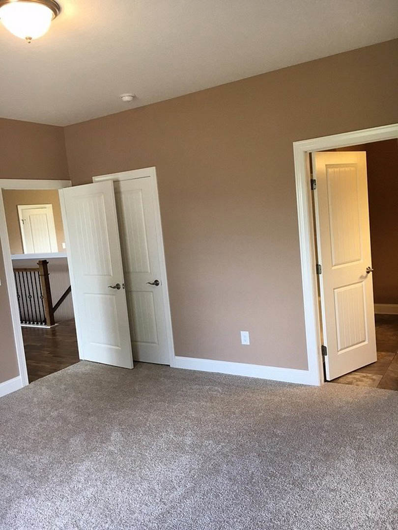 Carpeted room featuring two white doors with silver handles, white walls with crown molding, and a close-up view of a staircase railing