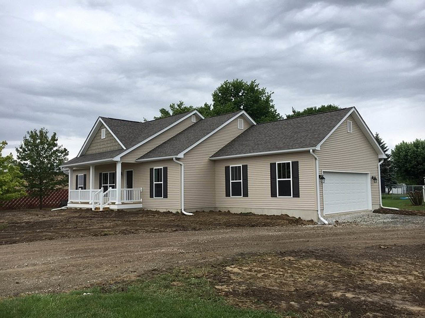 White-roofed house with a porch featuring white railings, garage door with side light, barred window, and dirt road bordered by trees; Robert Frost Farm visible in the background.