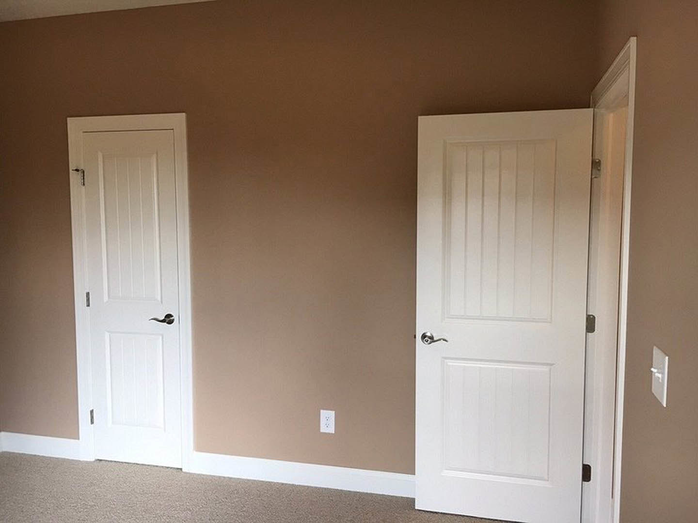 White paneled doors with silver handles set in a neutral-toned room featuring smooth walls and light wood flooring