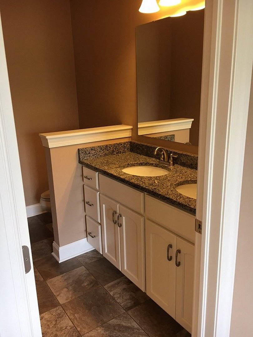 Bathroom featuring granite countertop, white cabinets, undermount sink, brown tile floor, and brushed nickel fixtures