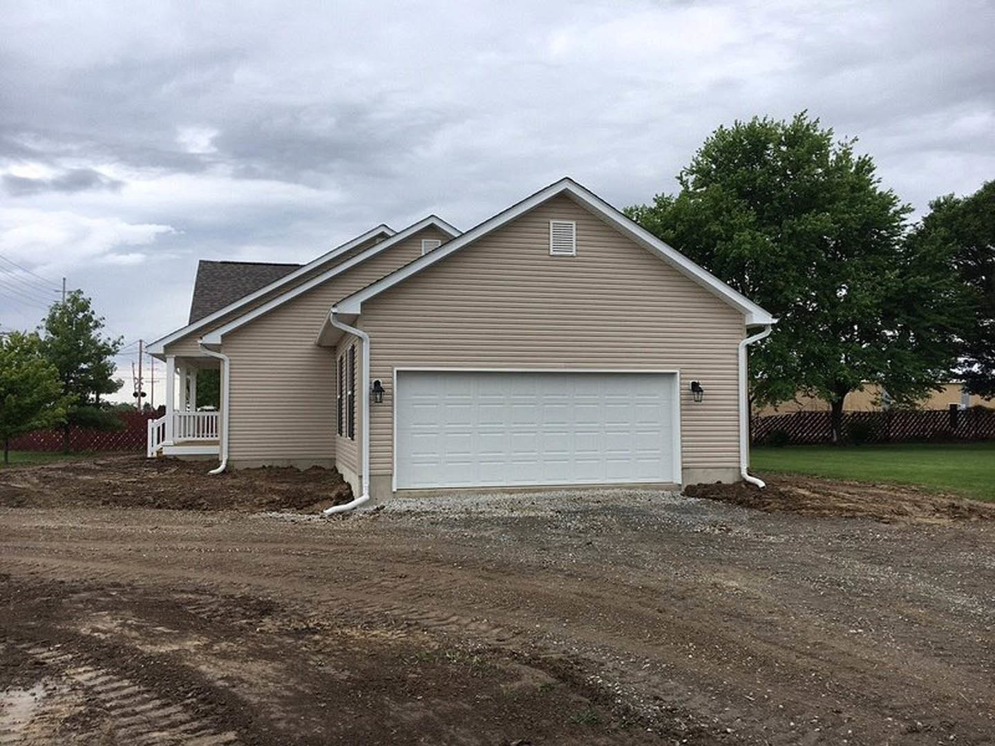 White garage door with brown trim on a residential home, tree beside the building, American Gothic House visible in the background, dirt road and white pipe in foreground, cloudy
