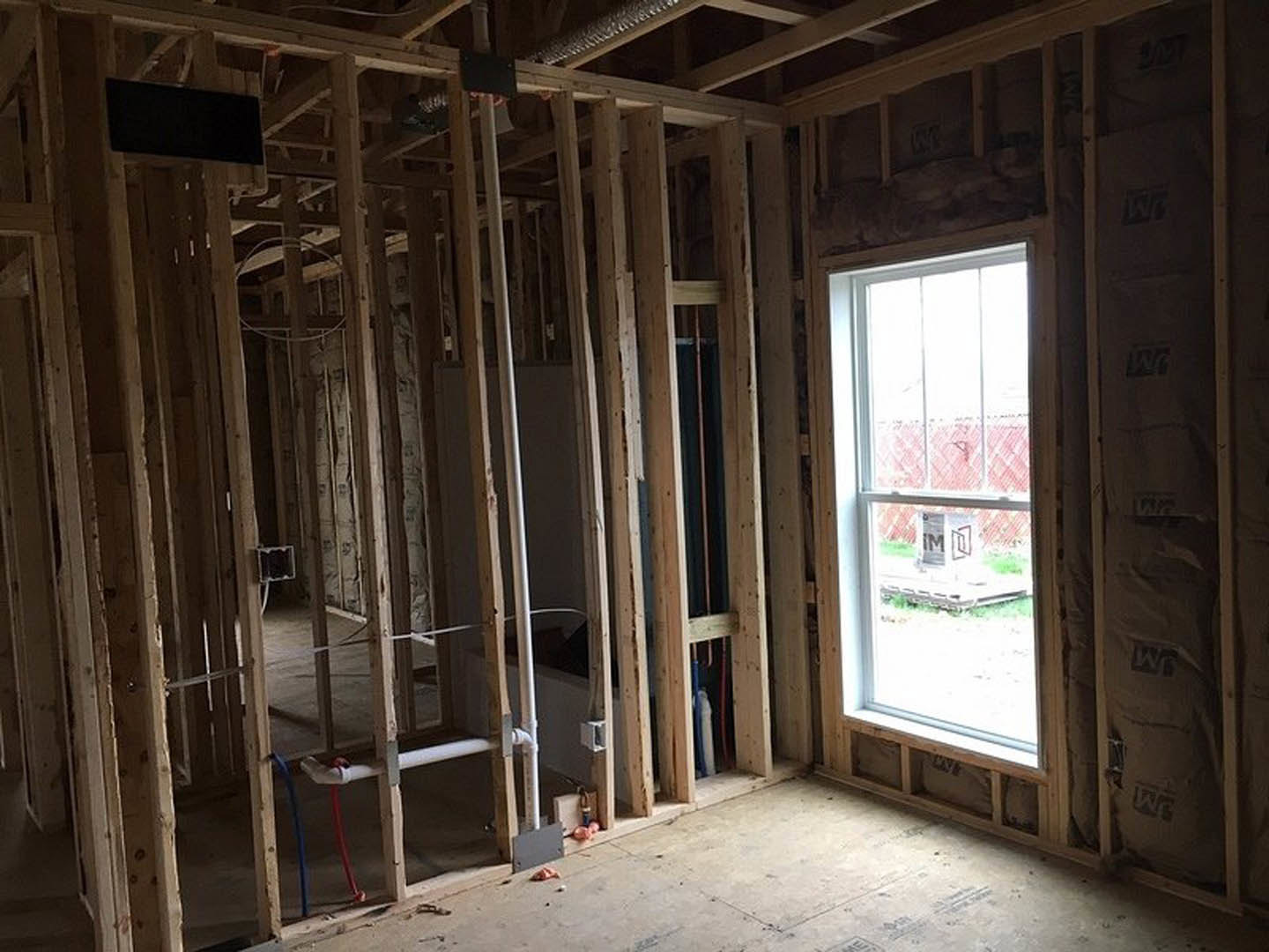 Unfinished room with exposed wood framing, window with a cardboard box on sill, black rectangular object resting on wooden beam, visible building insulation