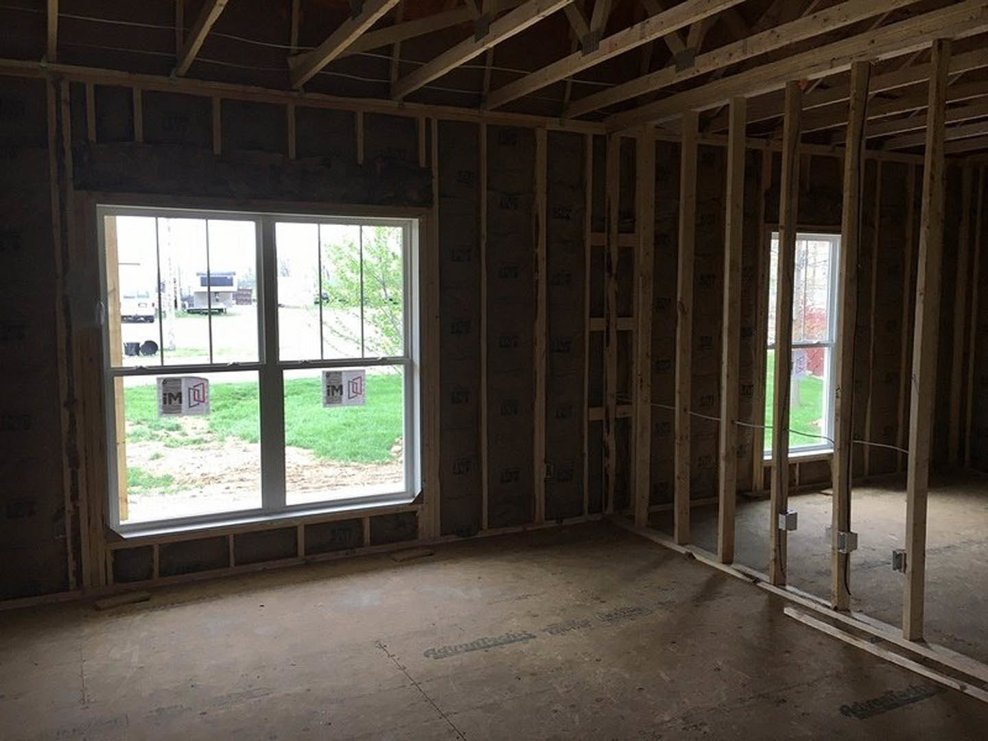 Wood-framed room with exposed ceiling beams, concrete floor, and large windows displaying construction signage