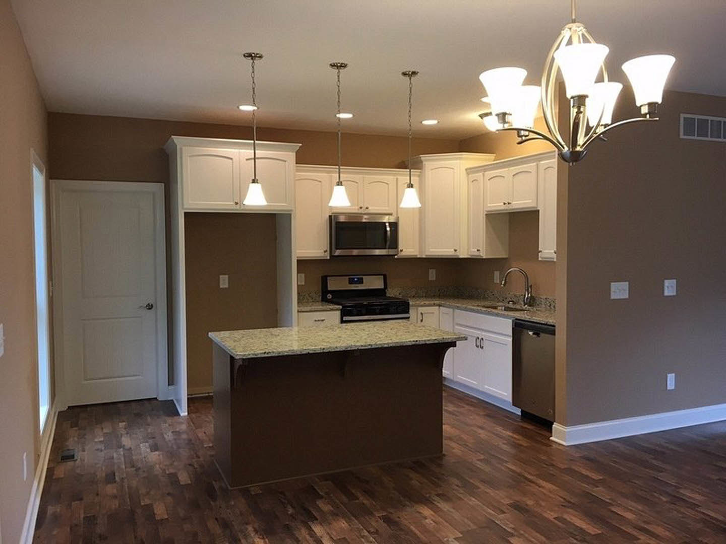 Open-concept kitchen featuring a central island with white quartz countertop, modern chandelier with four lights above, stainless steel microwave and oven built into white