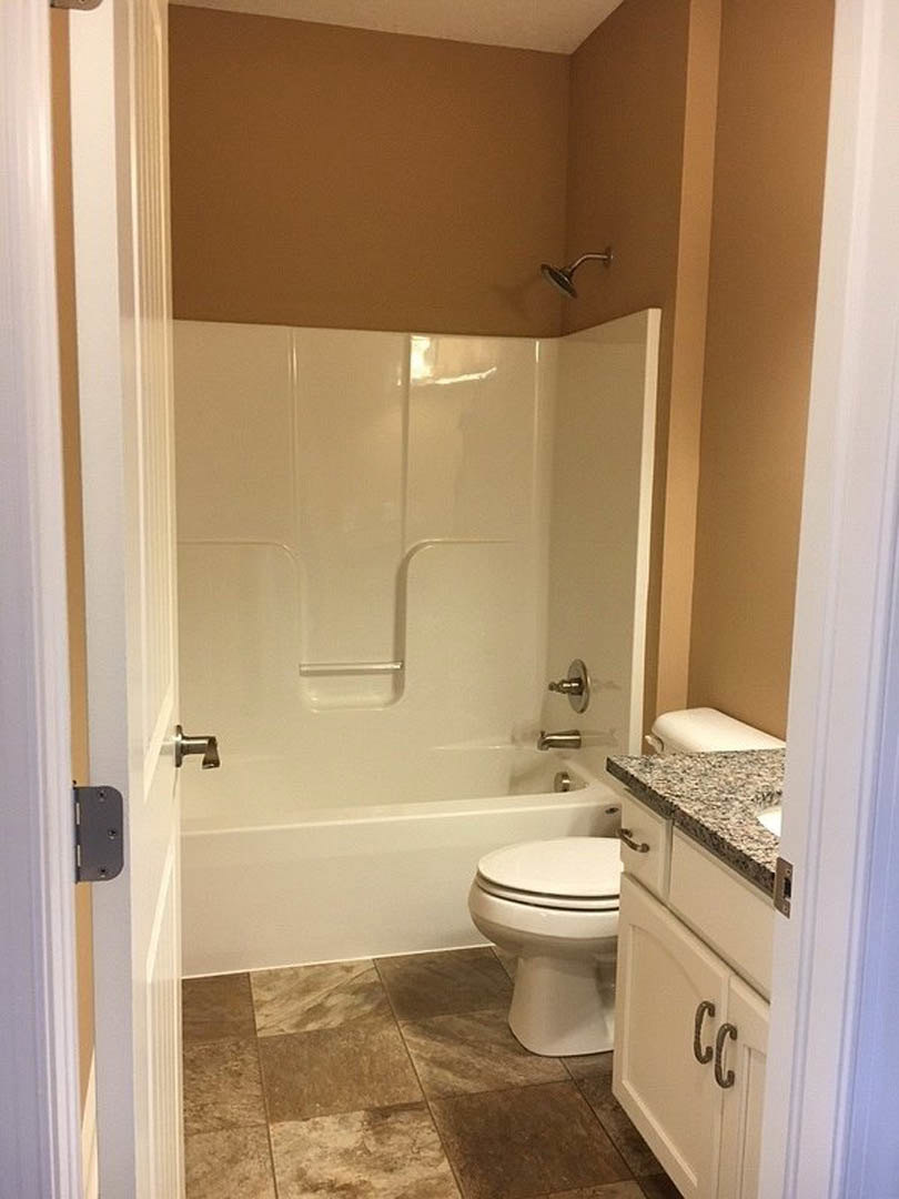 Bathroom with white toilet, glass shower enclosure, chrome showerhead, and brown tile flooring