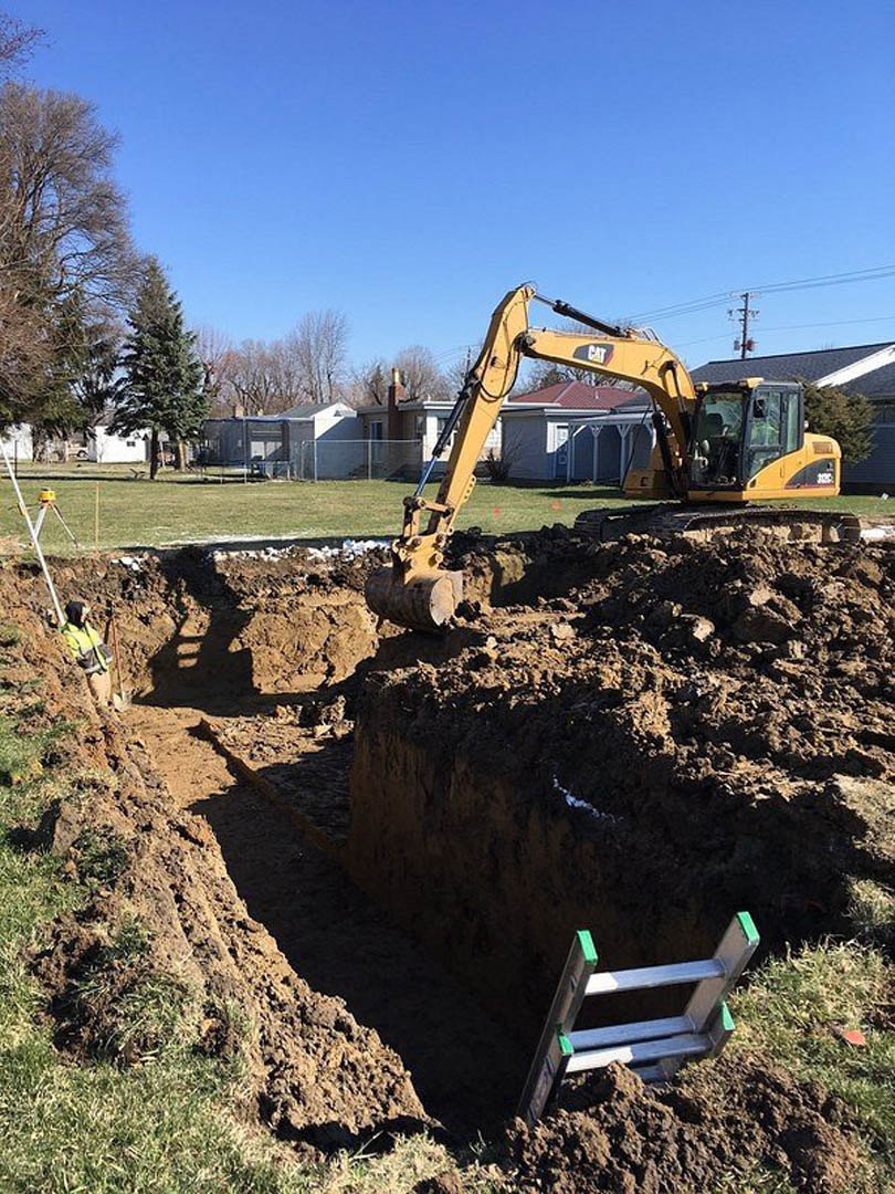 Bulldozer and ladder on dirt construction site beside leafless tree under open sky