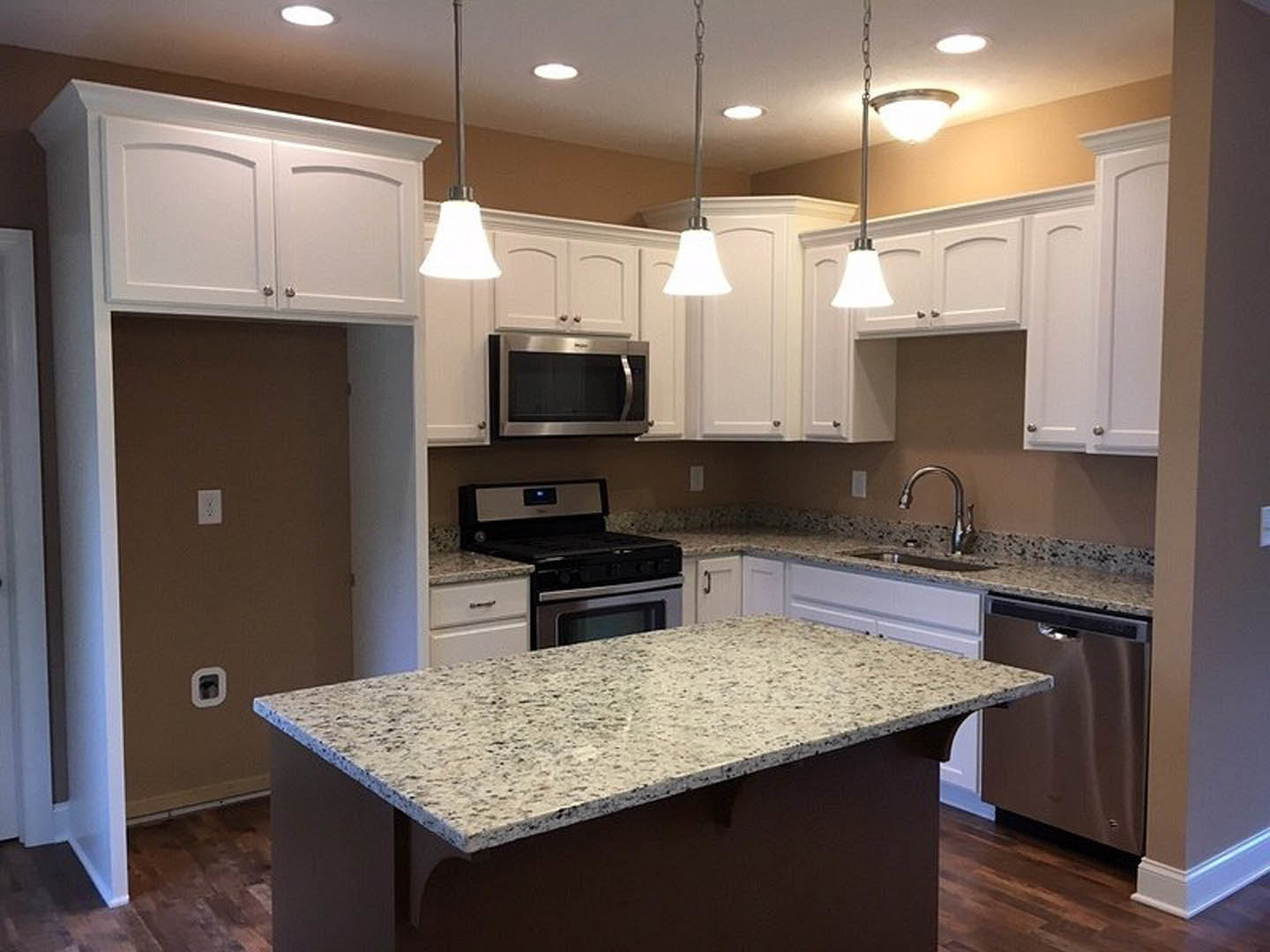 White kitchen with granite countertops, stainless steel stove and oven, built-in microwave, undermount sink with chrome faucet, and shaker-style cabinetry