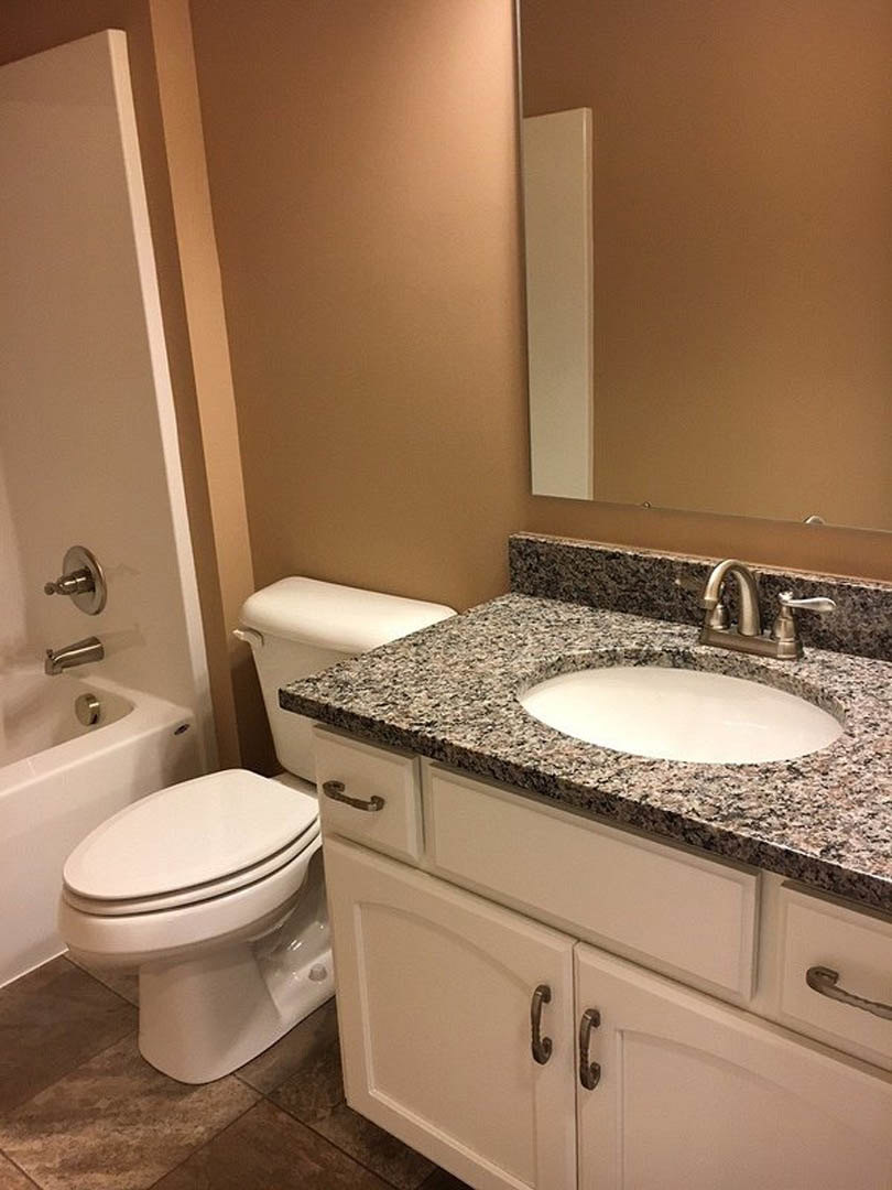 Bathroom with marble countertop vanity, undermount sink, chrome faucet, white toilet, light tile flooring, and neutral wall tiles