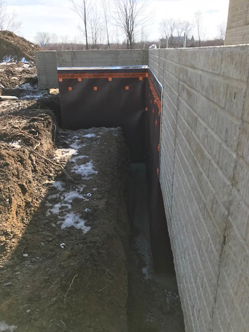 Excavated construction site with exposed brick walls, snow covering the ground, metal beam resting on wooden platform, and surrounding dirt