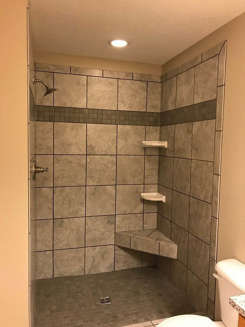 Walk-in shower with chrome shower head mounted on white subway tile wall, tiled floor with square drain, adjacent toilet, and partial view of tiled corner