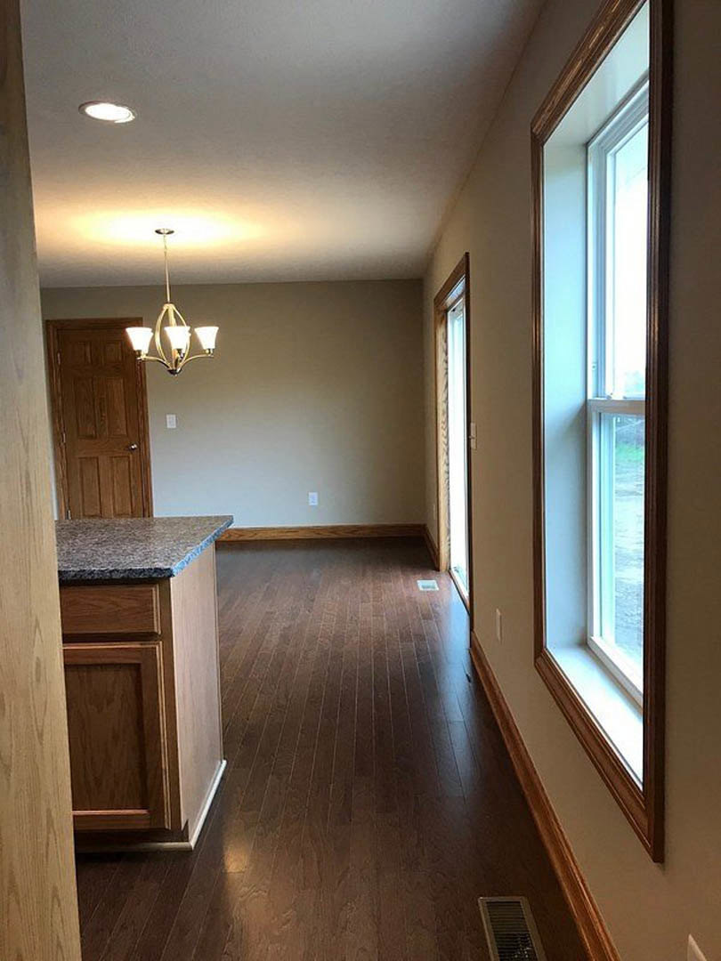 Hardwood floors in kitchen and dining area, white-framed window, ceiling light fixture, wooden cabinetry, wall vent, close-up of interior door