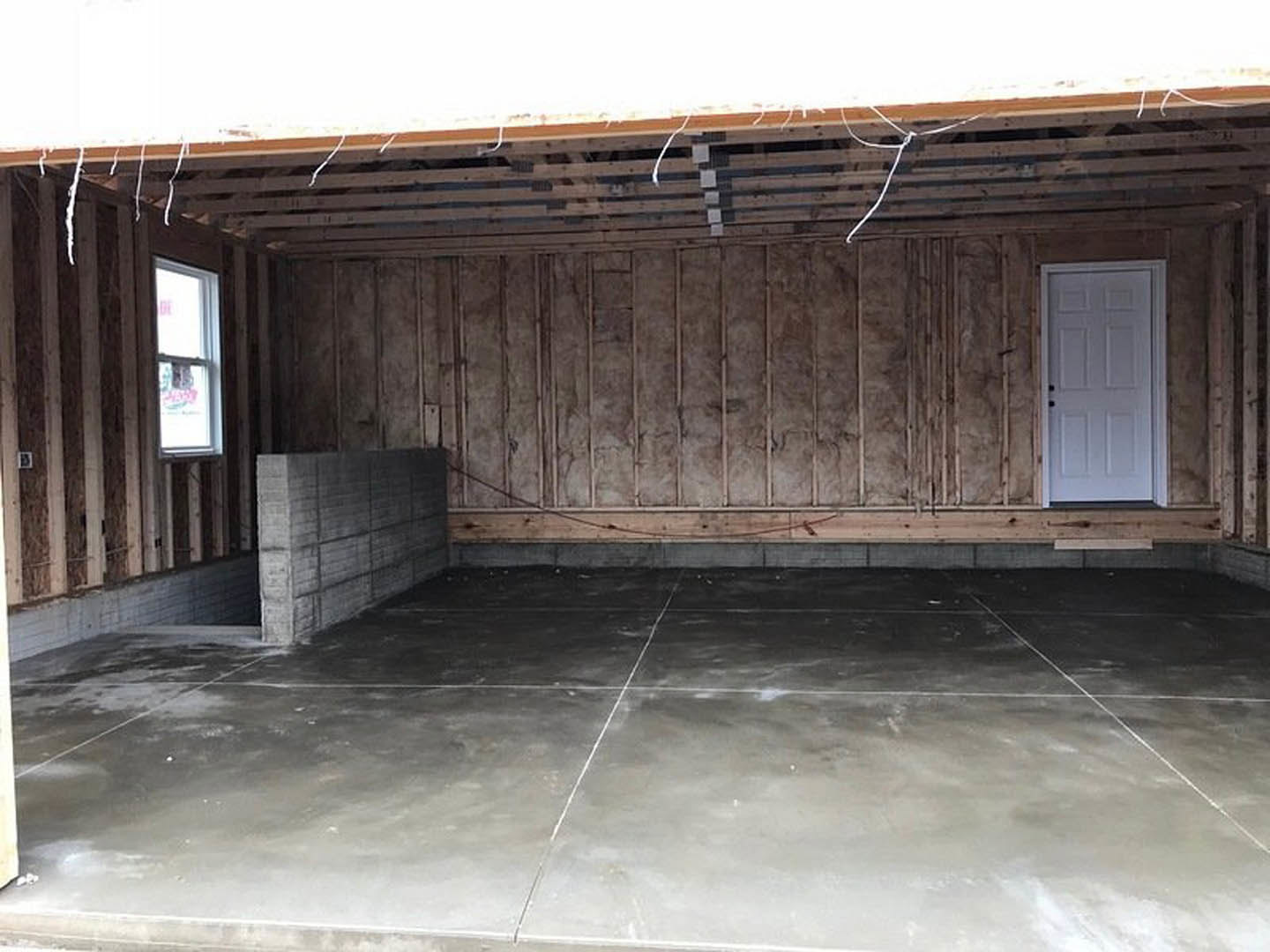 Polished concrete floor in a modern interior with white door featuring black knobs, white-framed window, and exposed wood beams.