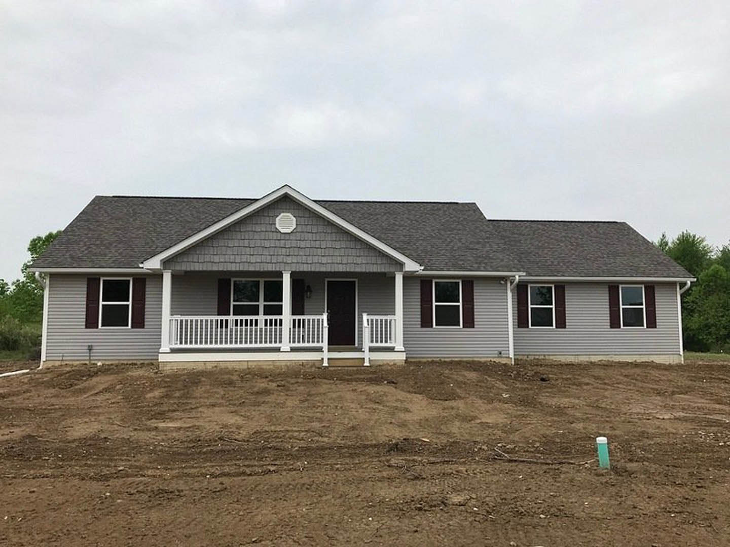 Two-story house with black roof, white porch railing, black front door with white frame, large windows, and a dirt patch covering the front yard.