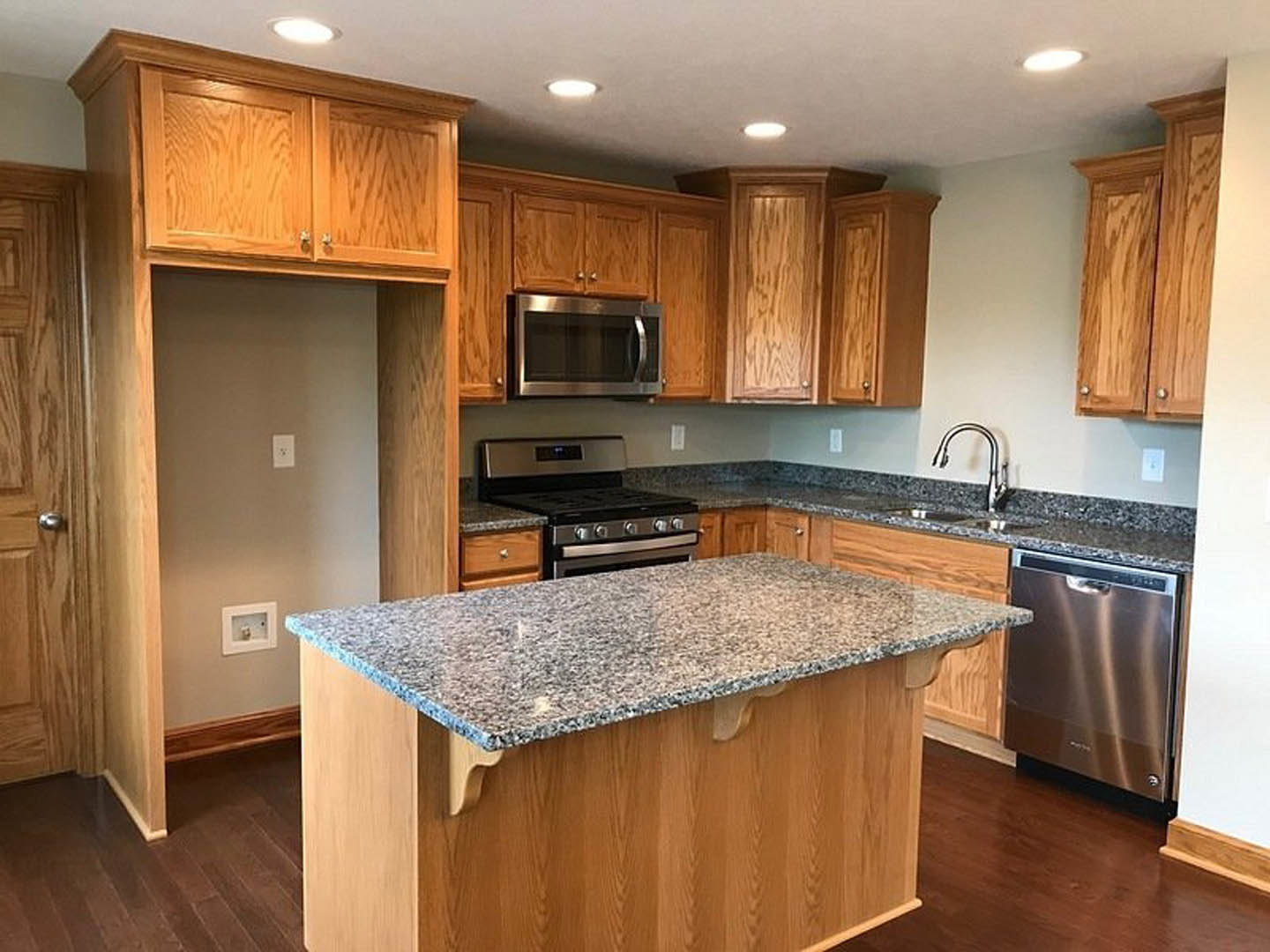 Granite kitchen island with stainless steel appliances, white cabinetry, and hardwood flooring