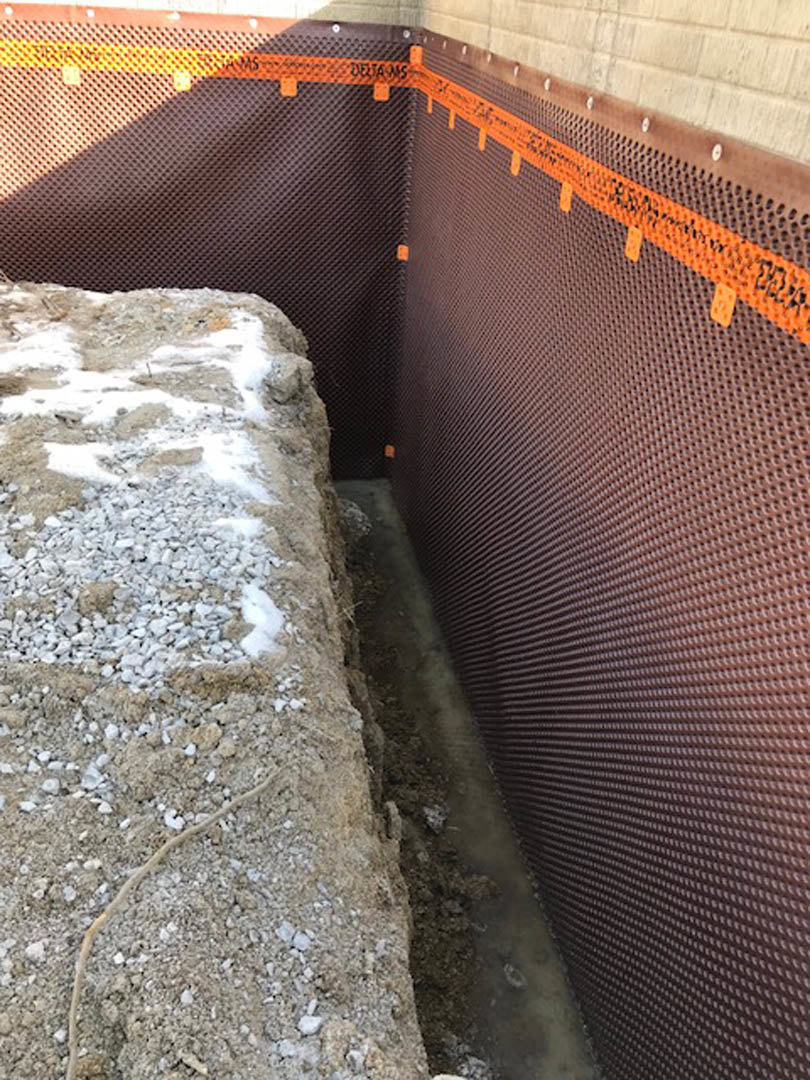 Rock and gravel landscaping beside an exterior composite wall, outdoor ground visible