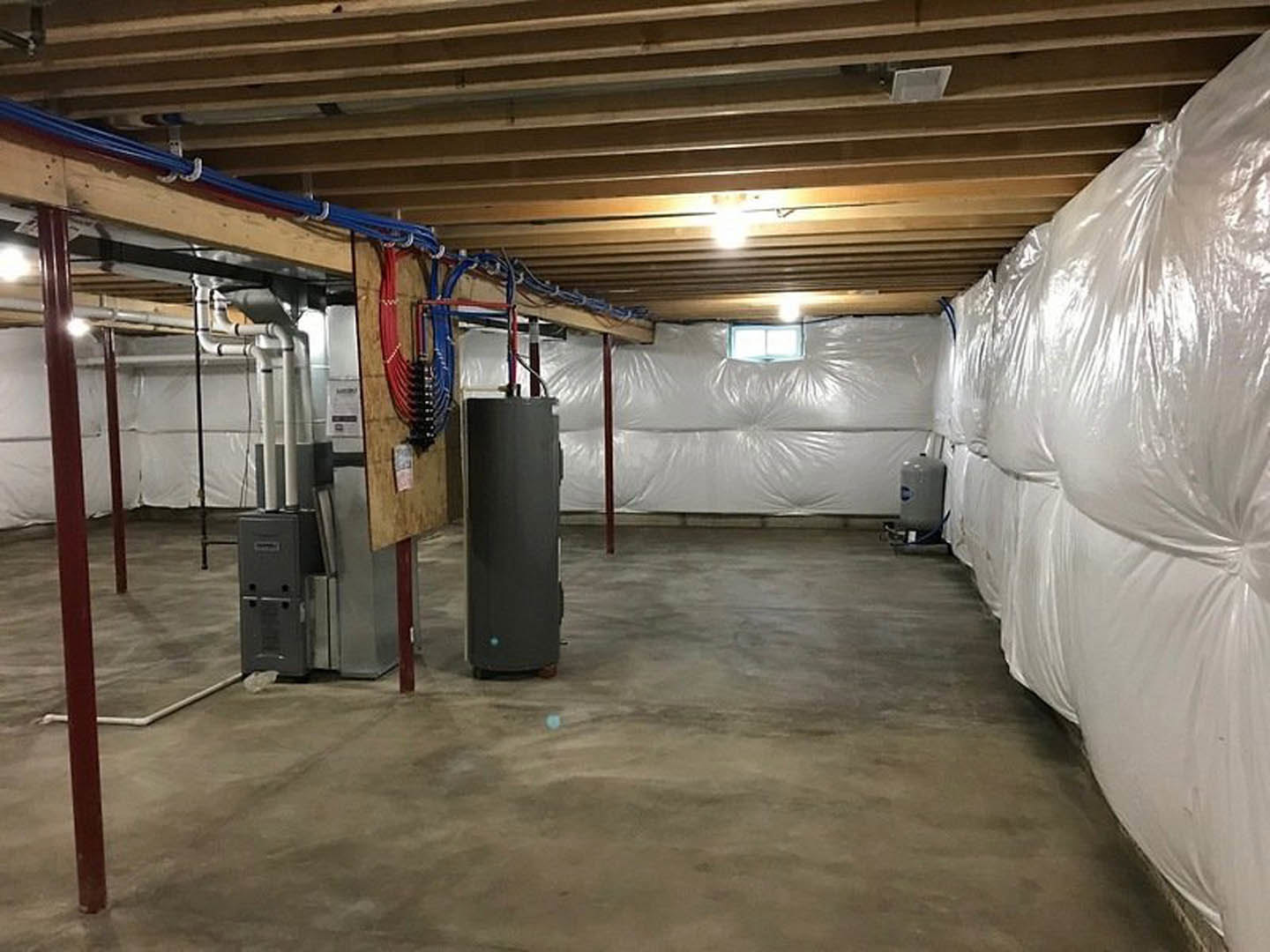 Large white plastic bag resting on unfinished basement floor, exposed ceiling with recessed lights and visible wiring, concrete walls, and scattered construction materials.