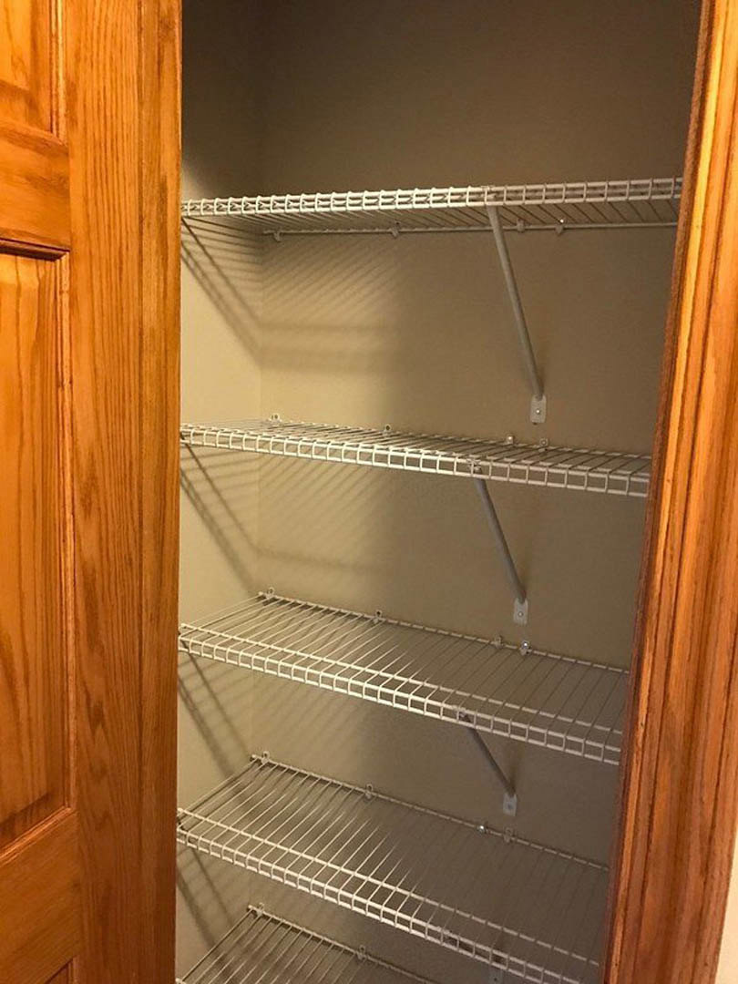 White wire shelving installed in a walk-in closet with wood grain cabinetry and neutral walls