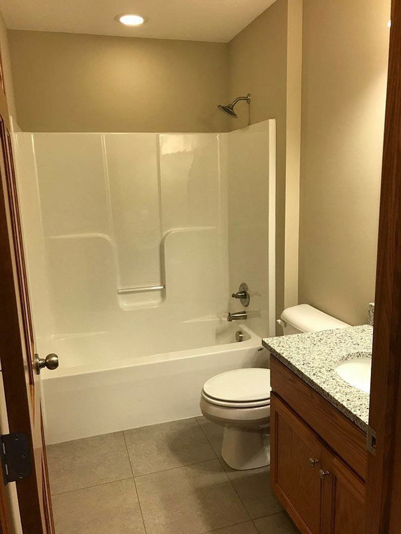 Bathroom with white tile walls, built-in bathtub, glass shower enclosure, chrome shower head, and modern white toilet.