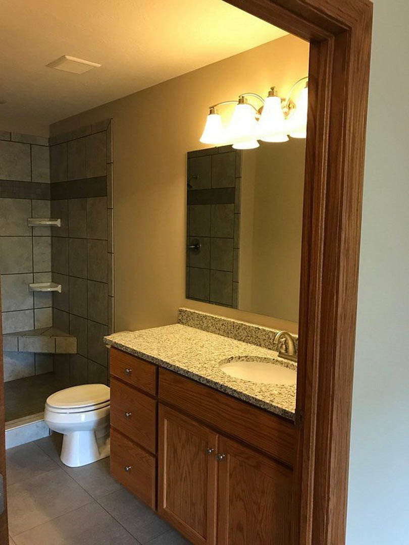 Bathroom with granite countertop vanity, undermount sink, white toilet, three-light fixture, tile flooring, and white ceiling vent