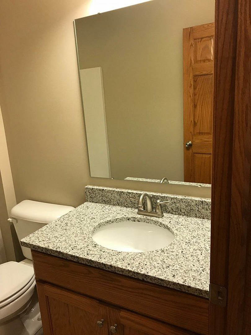 Marble countertop with white sink and chrome faucet, adjacent to a white toilet, light tile flooring, and partial view of a wooden door
