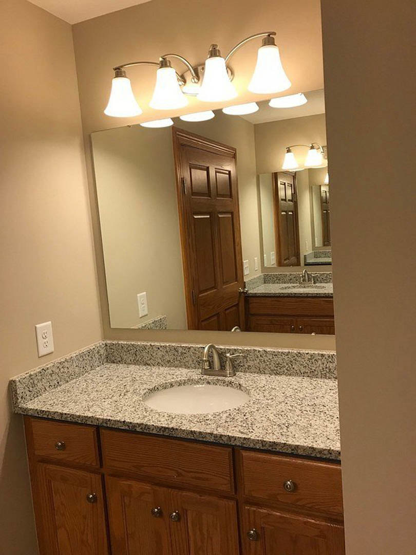 Marble countertop with undermount sink, chrome faucet, white cabinetry, and tiled backsplash in a modern bathroom