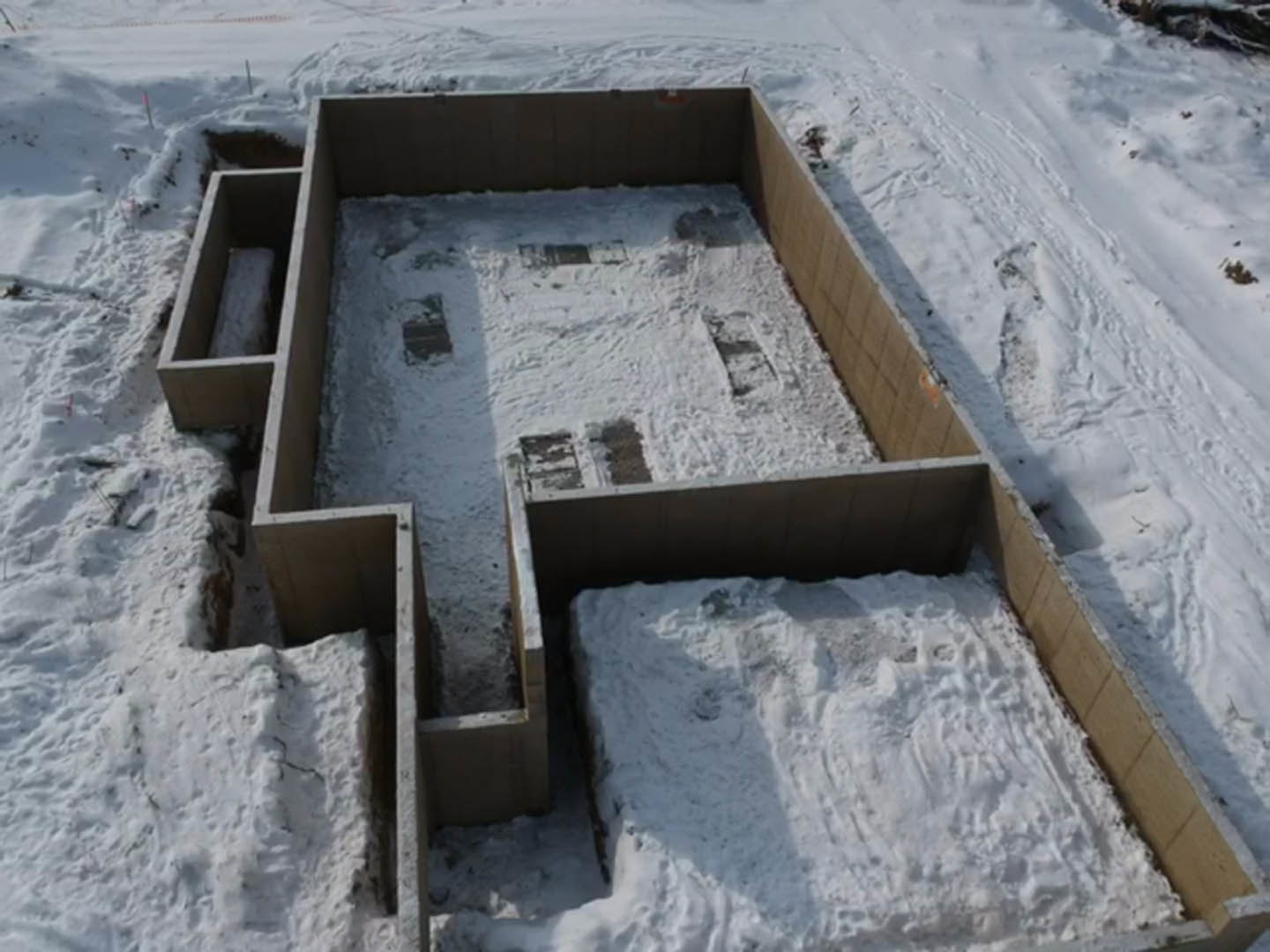 Modern home exterior with large windows and flat roof, surrounded by snow-covered ground and trees, under overcast winter sky