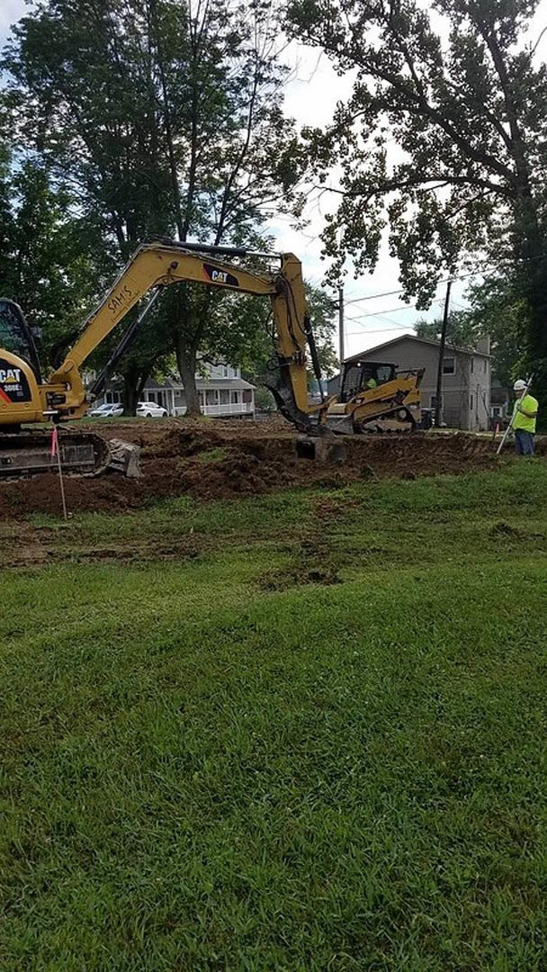 Bulldozer parked on grassy construction site beside man, with dirt excavation and trees in background