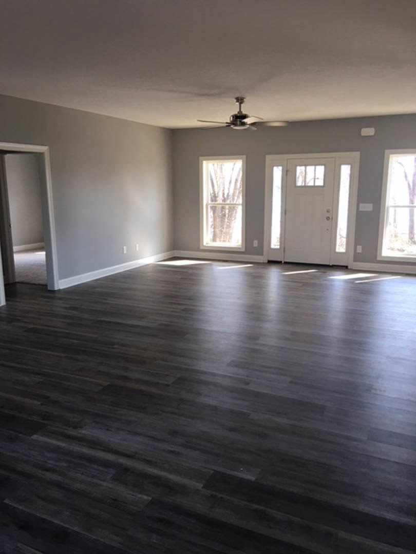 Room with dark hardwood flooring, white walls, white-framed window, white door with glass panes, and ceiling fan with light fixture