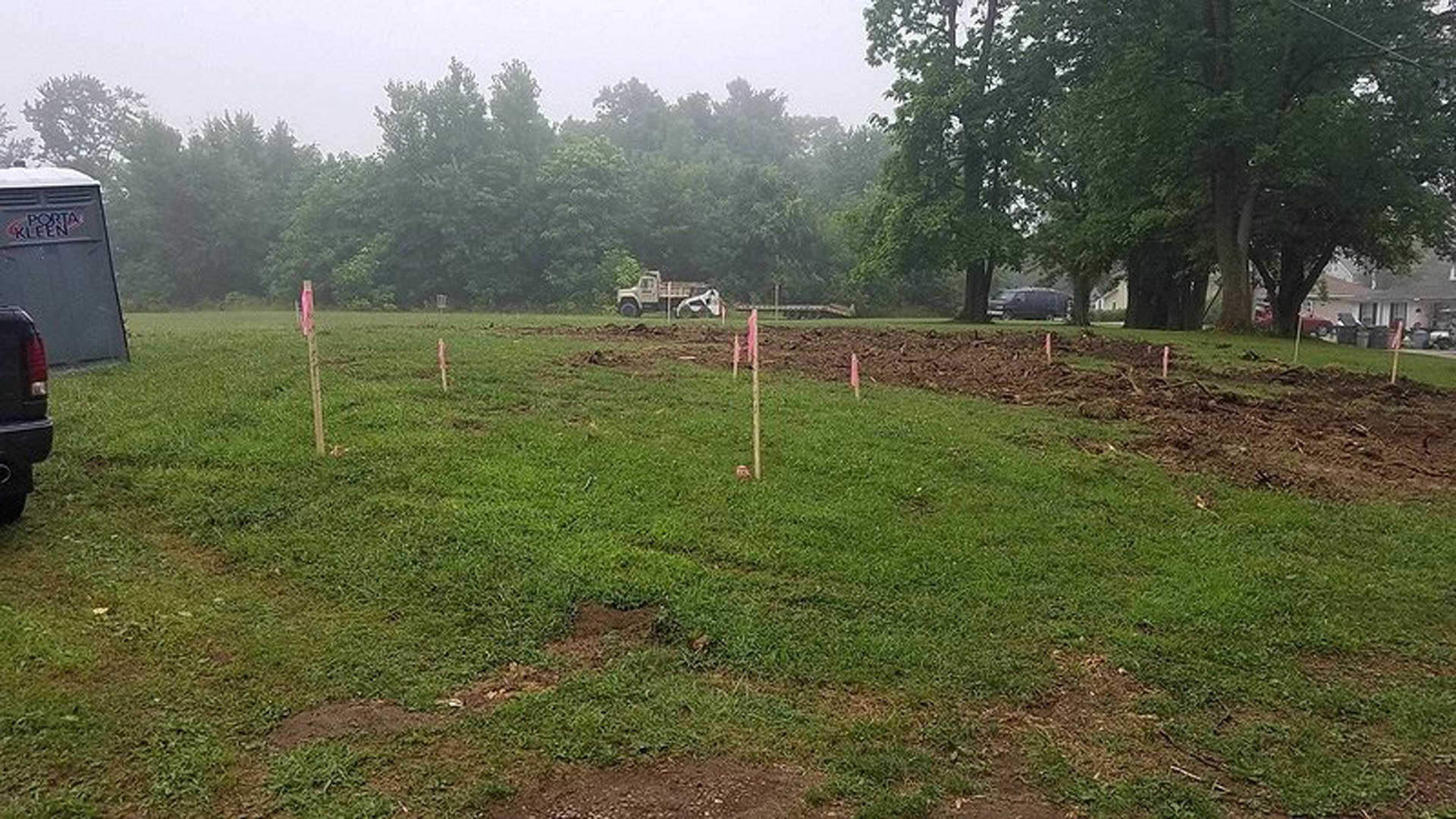 Grassy field with scattered utility poles, pickup truck parked near a partially visible building, blue sky overhead
