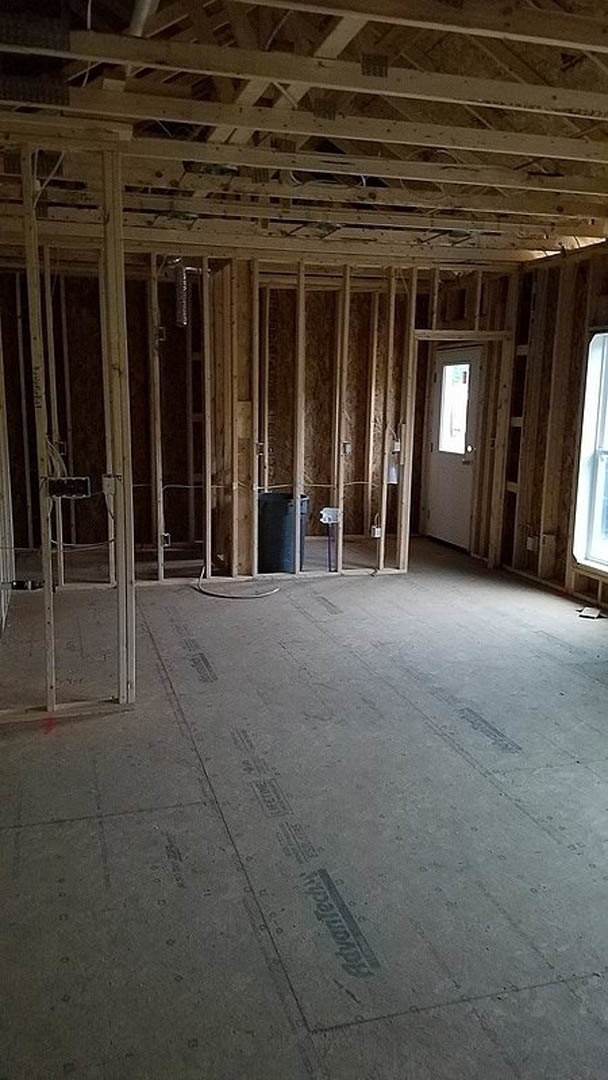 Exposed wood framing with ceiling beams, unfinished walls, construction insulation, and concrete floor in a residential interior.