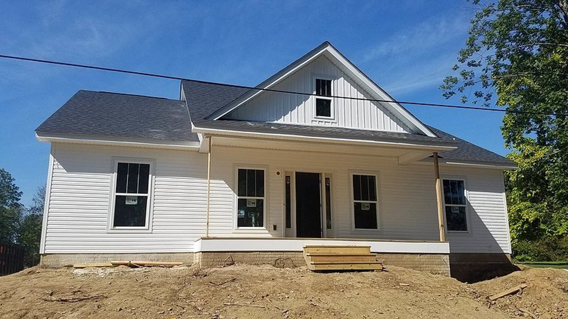Partially built house with exposed wood paneling, white-framed windows displaying construction signs, and several trees surrounding the exterior.