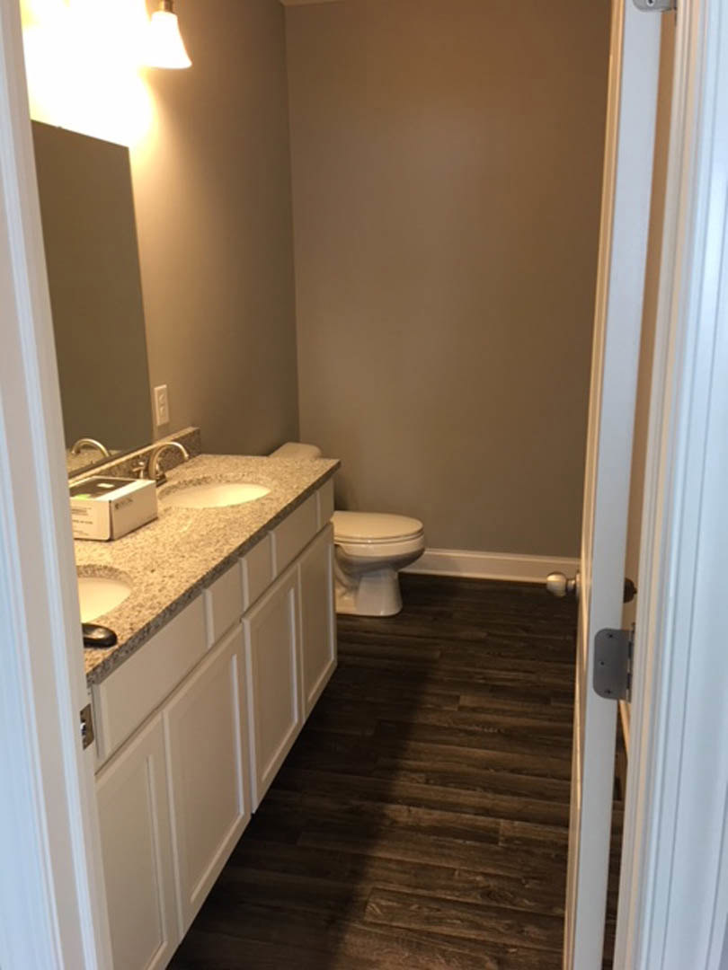 Modern bathroom featuring a white toilet, rectangular sink with chrome faucet, light gray tile flooring, and a wall-mounted mirror above the vanity.