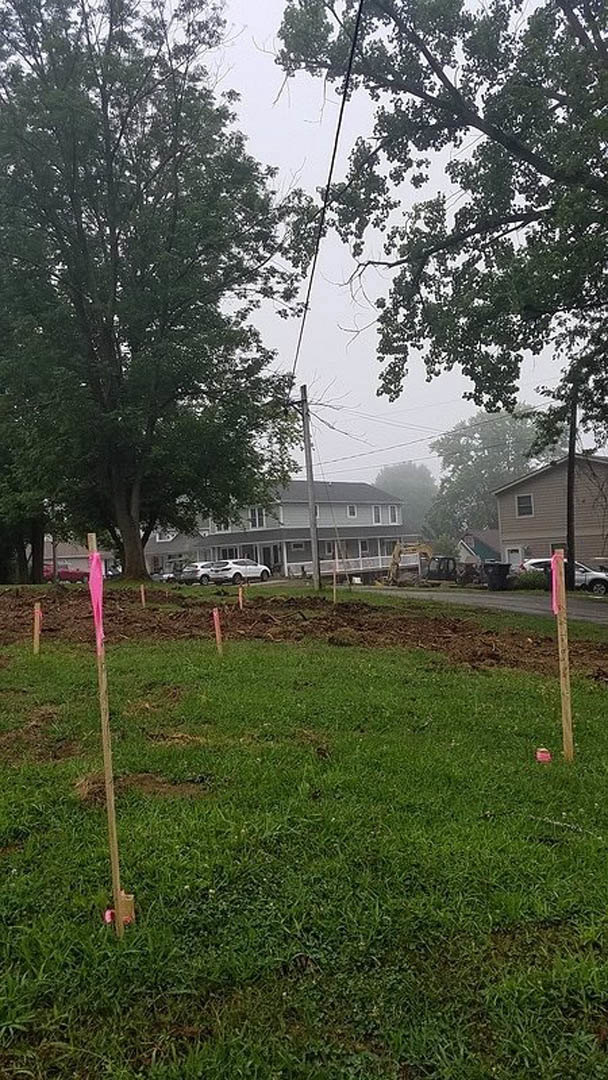 Grassy field with scattered pink flags, bordered by trees under a blue sky