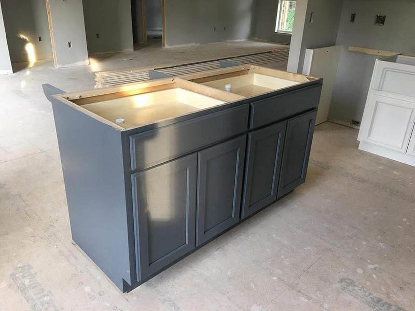 Quartz kitchen island countertop with built-in sink, white cabinetry and drawers, stainless steel appliances, light hardwood flooring, white walls with light switch and wall