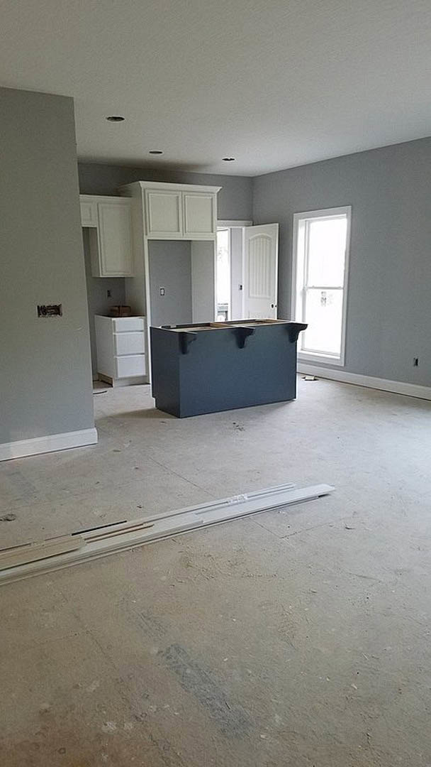 Modern kitchen featuring white shaker cabinets, light stone countertops, stainless steel appliances, wide plank wood flooring, and large windows with natural light.