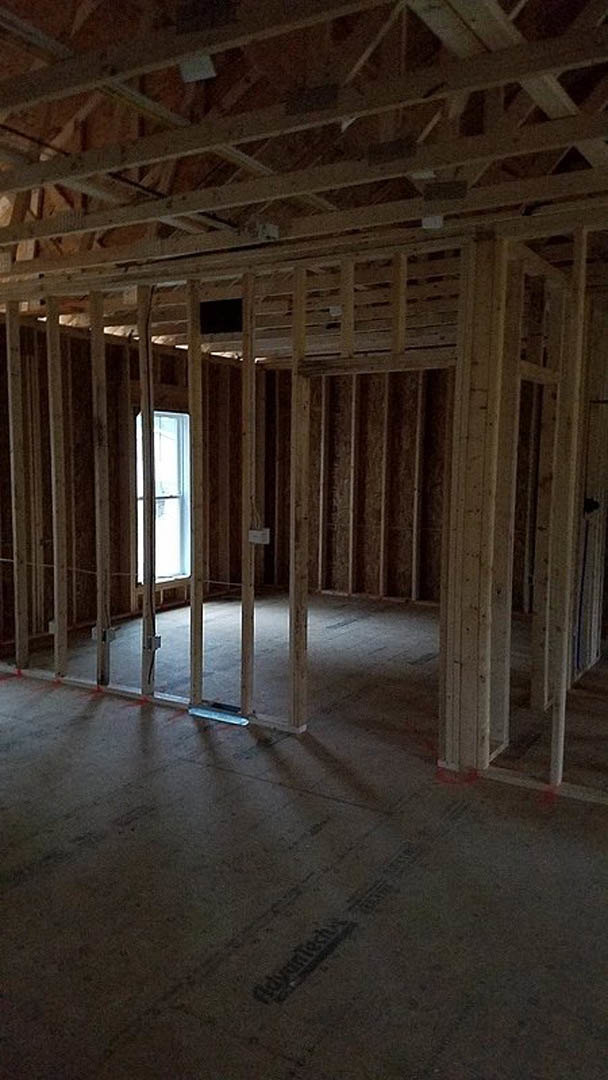 Room under construction with exposed wood framing, ceiling beams, unfinished floor, and window with visible window pane.